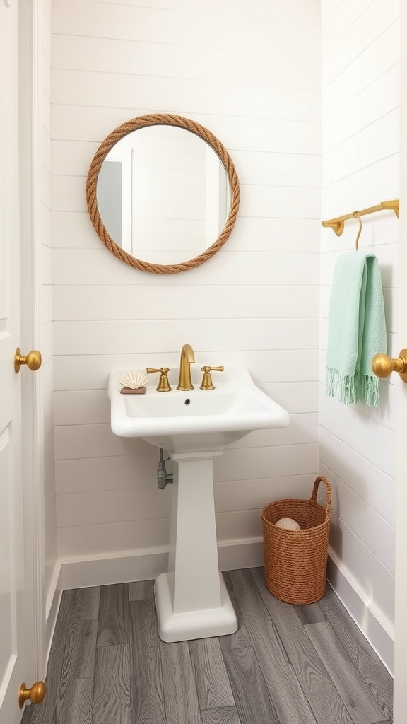 Coastal retreat bathroom with white shiplap walls, a pedestal sink, gold fixtures, a round mirror, and mint towels.